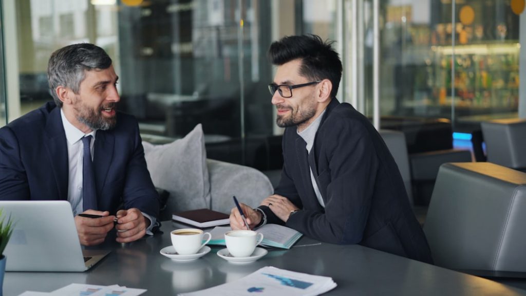 a-couple-of-men-sitting-at-a-table-in-front-of-a-laptop-0e5egrnj-ss